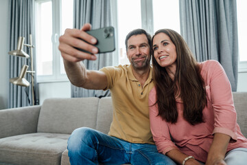 Smiling mature couple taking selfie in apartment