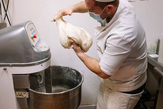 Mid adult chef preparing dough for bread by electric mixer in bakery during COVID-19