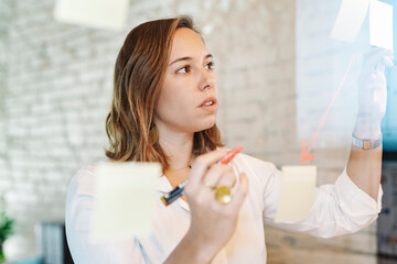 Close-up of businesswoman preparing business plan over adhesive notes stuck on glass wall