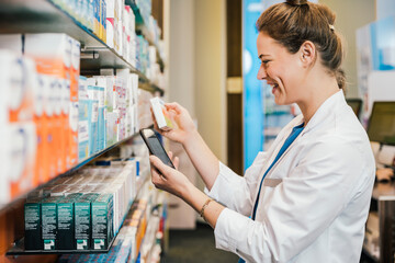 Happy pharmacist with smart phone checking medicine while working at pharmacy