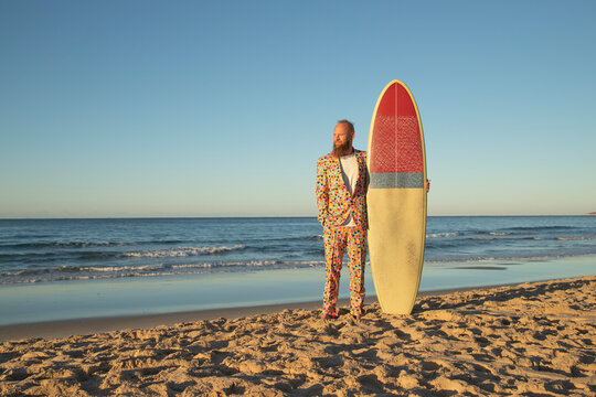 Fashionable man with surfboard looking away while standing against sea