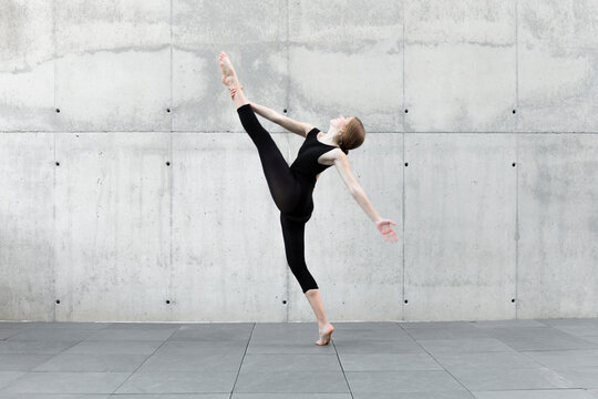 Dancer in black leotard dancing in front of concrete wall