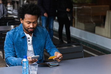 Mid adult man using credit card and smart phone for paying at sidewalk cafe