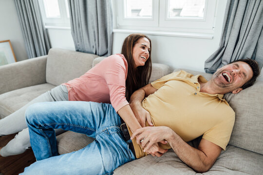 Happy mature woman tickling man while sitting on sofa at home