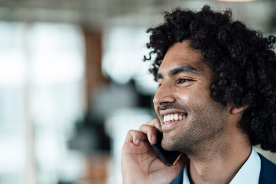 Cheerful Male Professional Talking On Mobile Phone While Looking Away In Office