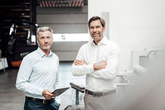 Businessman with digital tablet standing by partner at industry