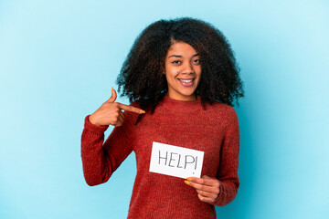 Young african american curly woman holding a help placard person pointing by hand to a shirt copy space, proud and confident