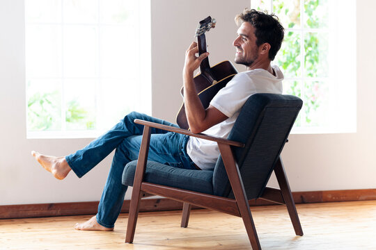 Mid adult man smiling while playing guitar at home