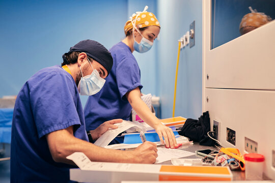 Assistant wearing face mask writing in paper while working by nurse at hospital