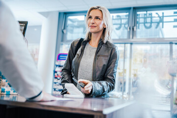 Smiling customer making payment through smart phone at checkout counter in chemist shop