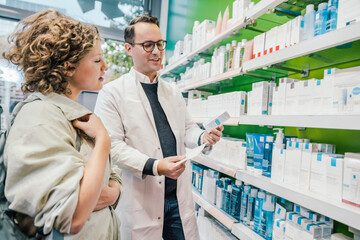 Fototapeta na wymiar Pharmacist recommending medicine to smiling customer in chemist shop