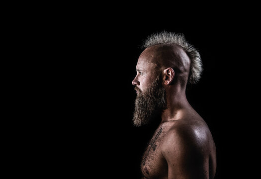Male viking with mohawk hairstyle standing against black background