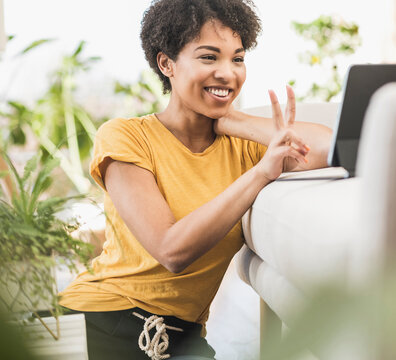Smiling woman showing peace gesture on video call through digital tablet while sitting at home