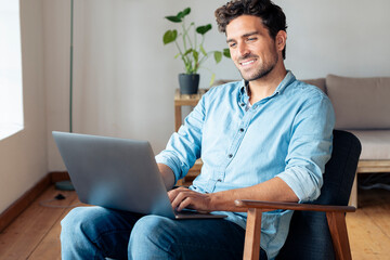 Smiling man using laptop while sitting on armchair at home