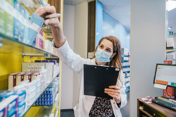 Female pharmacist wearing protective face mask while working in chemist shop