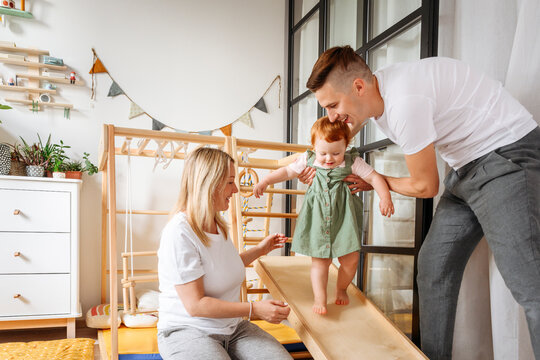 Parents assisting baby daughter walking at home