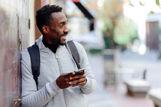 Man with backpack and mobile phone looking away while leaning on wall