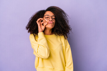 Young african american curly woman isolated on purple background with fingers on lips keeping a...