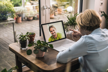 Grandmother gesturing while talking to grandson on video call through laptop on table at home