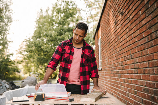 Man looking at toolbox while working by brick wall during summer