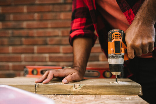 Midsection of man using drill machine on plank while renovating during summer