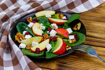 Autumn spinach salad with apple, feta cheese, walnut and dried cranberry on wooden table. Healthy vegetarian food