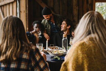 Smiling men talking while sitting with friends at dining table during social gathering