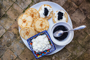 blinis with sour cream and caviar served on a plate on a ceramic garden table. traditional russian...
