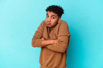 Young african american curly man isolated on blue shrugs shoulders and open eyes confused.