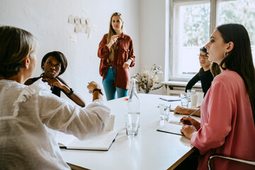 Female entrepreneur communicating on conference table with colleagues during workshop in office