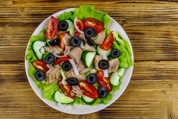 Tasty tuna salad with lettuce, black olives and fresh vegetables on wooden table. Top view