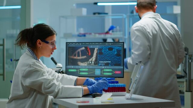 Team of microbiology scientists discussing about virus development in modern equpped laboratory using computer analysing test blood samples and develop vaccine, drugs and antibiotics against covid-19.