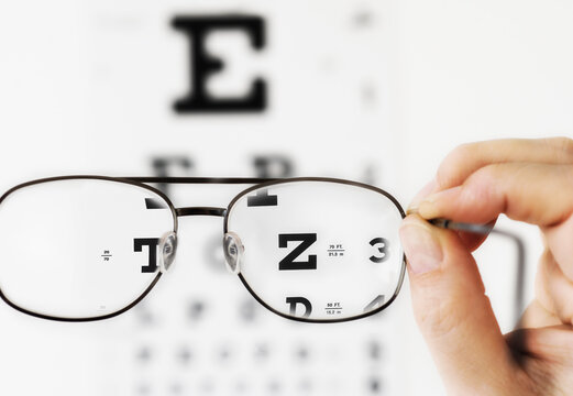 Close up of hand holding glasses above eye chart, studio shot