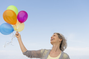 Senior woman holding bunch of colorful balloons