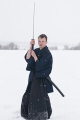 samurai warrior stands with sword and staff in the middle of an empty winter field