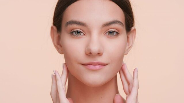 Close-up beauty portrait of young woman who gently touches and strokes her face skin from under eyes to the neck and looks at the camera | Eye cream commercial concept