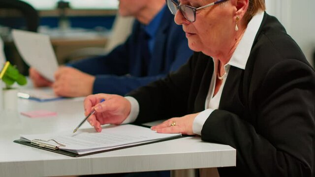 Busiess partners discussing new project for company evolution, senior manager woman checking tasks on clipboard and signing new contract. Executive director meeting shareholders in start up office