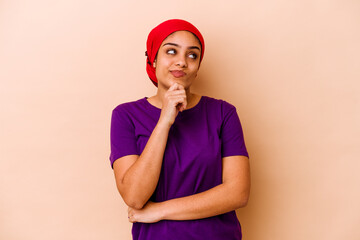 Young african american woman isolated on beige background thinking and looking up, being reflective, contemplating, having a fantasy.