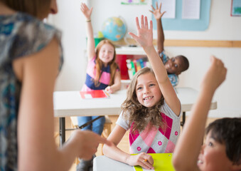 Children (8-9) raising hands in classroom