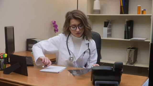 Young female doctor examines chest x-ray in her office and takes notes