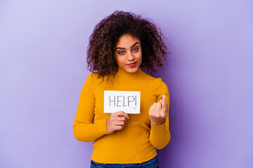 Young African American woman holding a Help placard isolated on purple background pointing with finger at you as if inviting come closer.