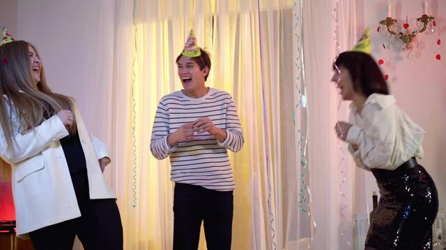 Joyful Caucasian millennial woman piercing balloon as man blowing it. Positive cheerful friends preparing birthday party indoors and having fun. Lifestyle and leisure concept.