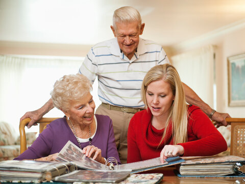 Senior couple and mid adult woman watching family scrapbooks