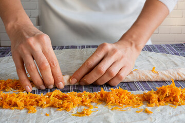 Pumpkin patty. On the table in the kitchen, wrapping candied grated pumpkin in filo pastry and preparing it for baking.