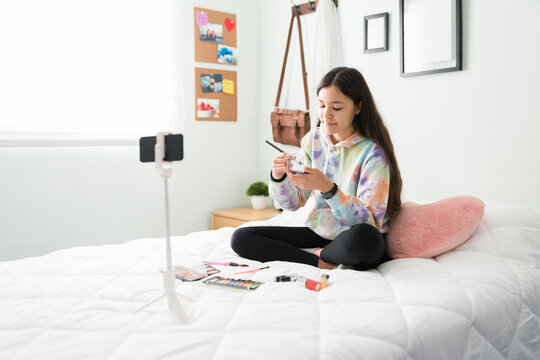Cute teen influencer filming a makeup tutorial in bed