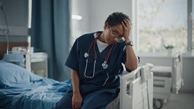 Hospital Ward: Portrait of Sad, Tired Black Nurse Sitting on a Bed, Holding Her Head in Sorrow for all the Patients that Couldn't Be Saved in Pandemic. During Tragic Times Brave Paramedics Save Lives