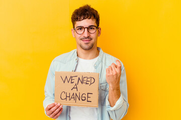 Young caucasian man holding a we need a change placard isolated pointing with finger at you as if inviting come closer.