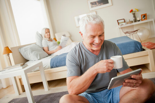 Senior man holding mug, woman sitting on bed in background - Powered by Adobe