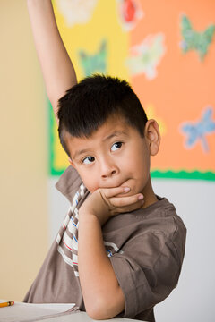 Boy (6-7) in a classroom with hand raised