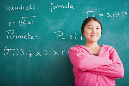 Happy Asian girl standing against blackboard after solving mathematical equation